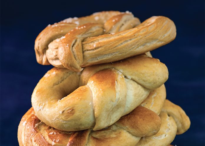Essential Pretzel Dough recipe with shaped pretzels stacked on blue surface