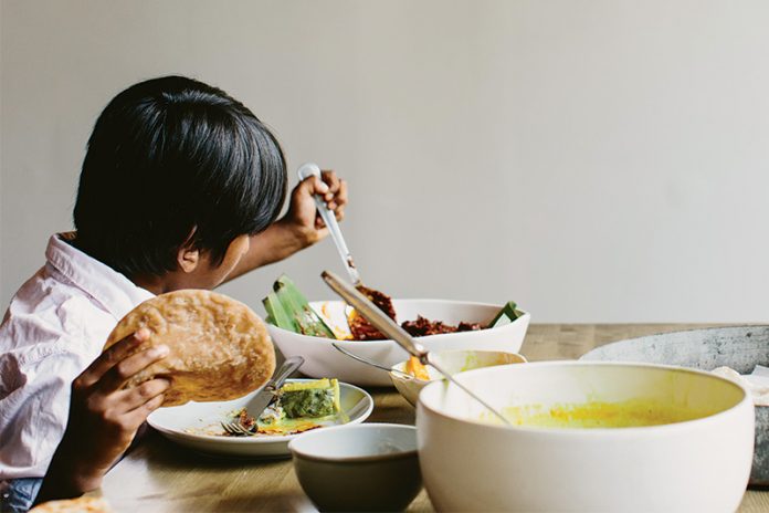 child holding roti while making a plate at the table