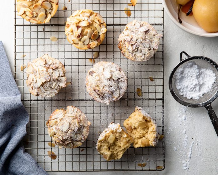 A close-up view of Champagne Poached Pear Muffins beautifully arranged on a wire rack, showcasing the muffins' golden-brown tops and chunks of poached pear elegantly placed on each muffin