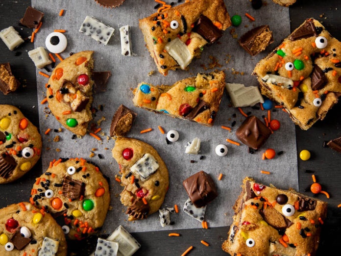Leftover Candy Compost Cookies & Bars on white parchment on black surface with fun sprinkles and candy scattered on surface