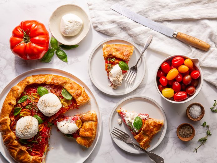 visual representation of a Three Cheese & Tomato Crostata from Bake from Scratch. The crostata is skillfully crafted, with a golden, flaky crust embracing a rich filling of three cheeses and ripe tomatoes. The dish showcases a harmonious blend of textures and colors, inviting anticipation of a delicious culinary experience