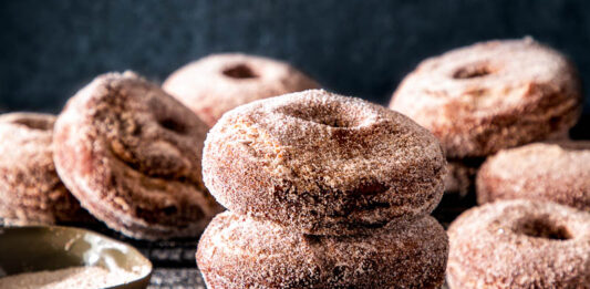 Spiced Apple Cider Doughnuts Spiced apple cider doughnuts on dark surface with cinnamon sugar spread