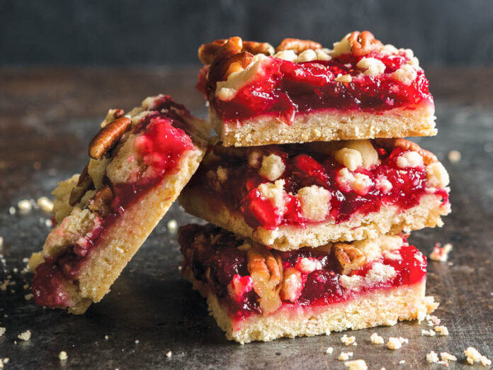 cranberry jam pecan bars stacked on dark surface.