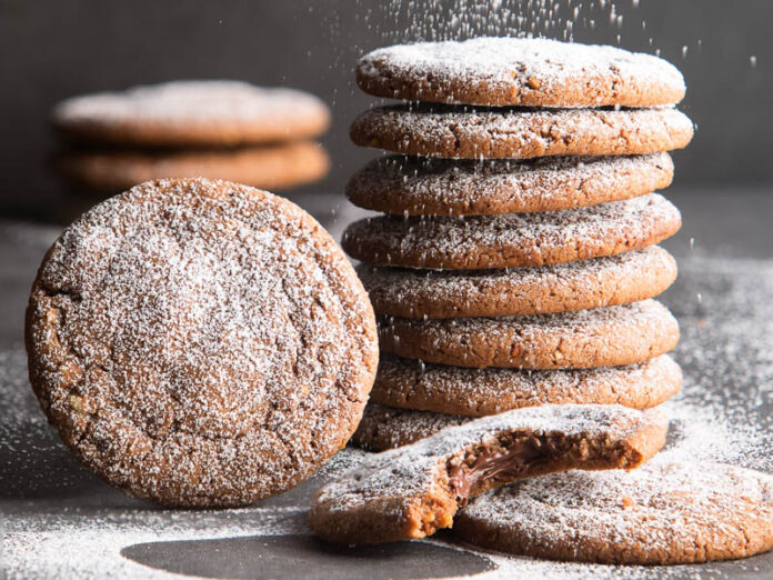 stuffed hazelnut chocolate cookies with powdered sugar being sprinkinled on top.