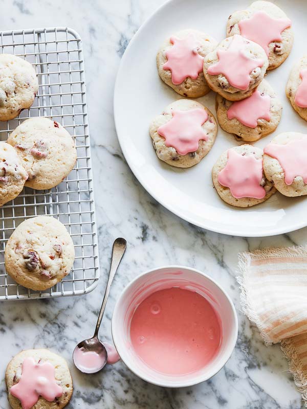 Glazed Campari & Strawberry Cookies on Plate and Wire Cooling Rack on Marble with Bowl of Glaze and Spoon