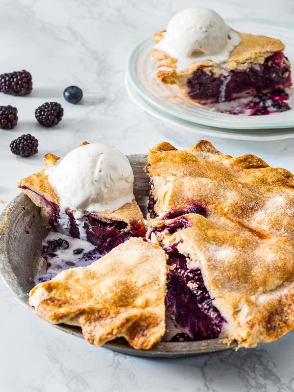 Berry Pie in a silver pie tin with a scoop of ice cream and a slice of pie on a white plate with blackberries and blueberries