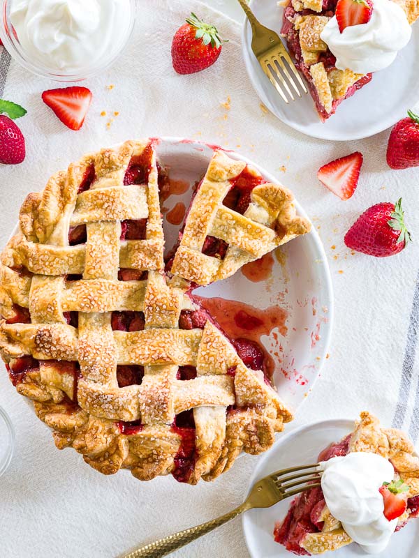 Strawberries & Cream Pie in white pie dish with strawberries and slices on white plates with forks and bowl of cream