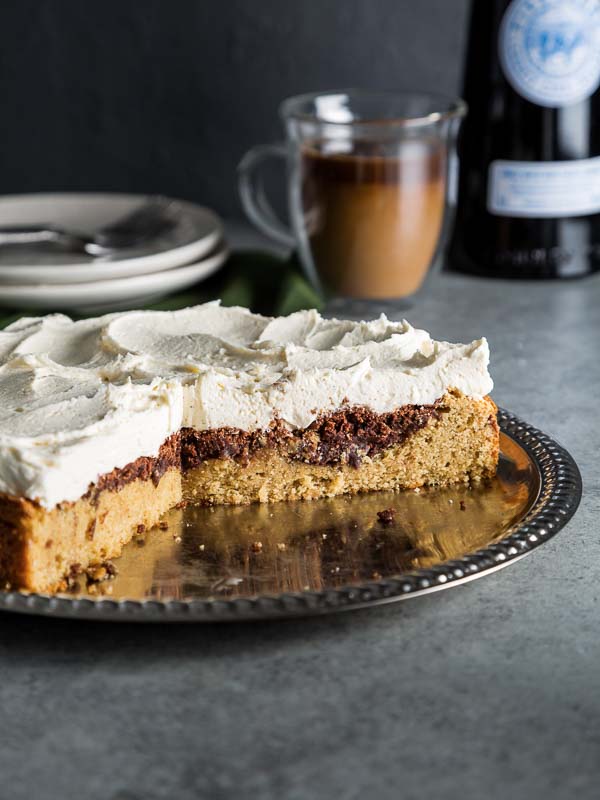 Irish Cream Cake on silver platter with cup of coffee and spirits in background with plates and forks