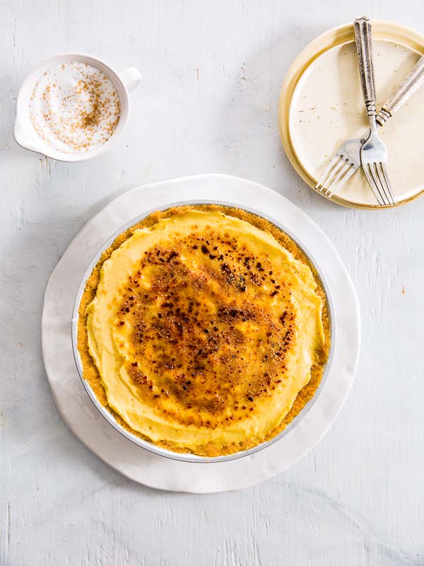Orange Blossom Vanilla Brown Sugar Pie on white platter with gold plate, two forks, and cup of sugar